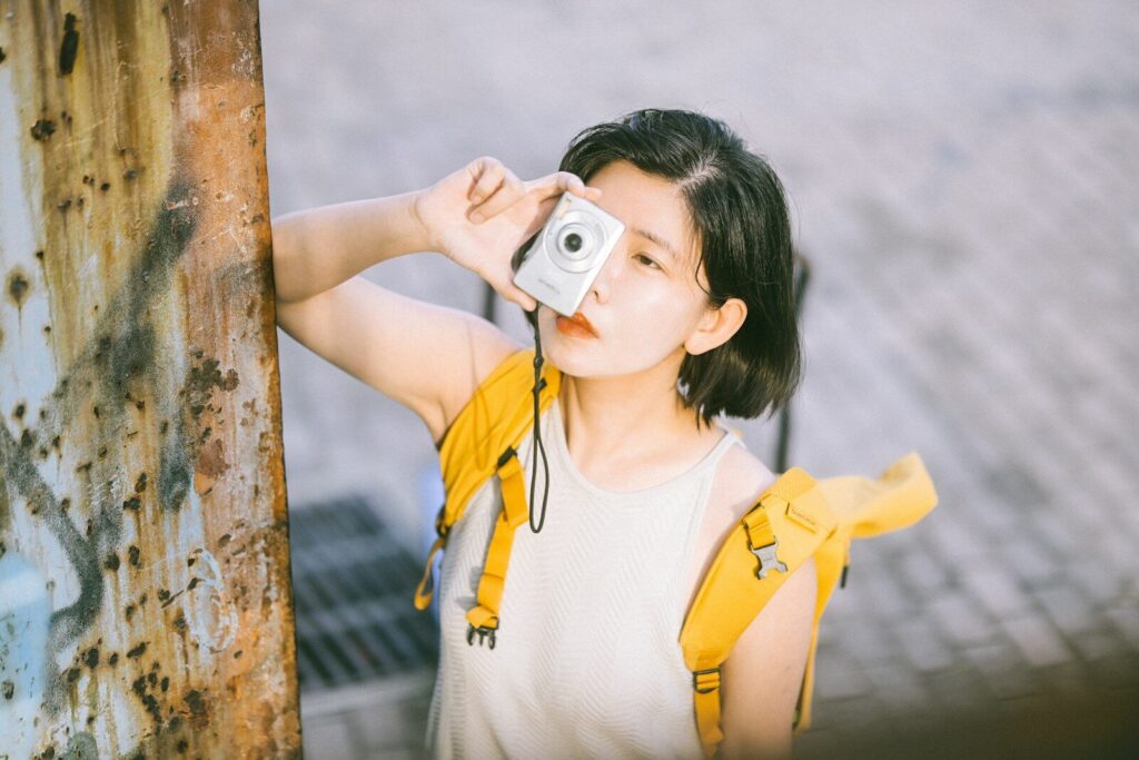 A woman with a yellow backpack holding a small silver camera to her eye